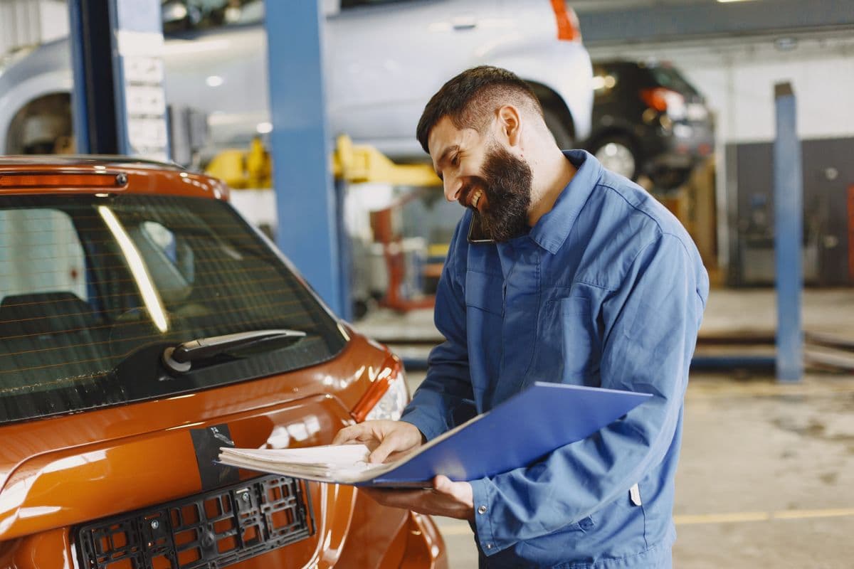 Mechaniker in der Werkstatt mit den Wartungsunterlagen eines Fahrzeugs
